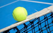 Una pallina da tennis sul nastro della rete e un campo da tennis blu